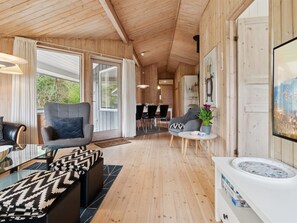 A modern interior with wooden walls and floors, a sofa, a chair, a dining area, and a large window. - "Apelun" - 60m from the sea by Interhome (Nexø)