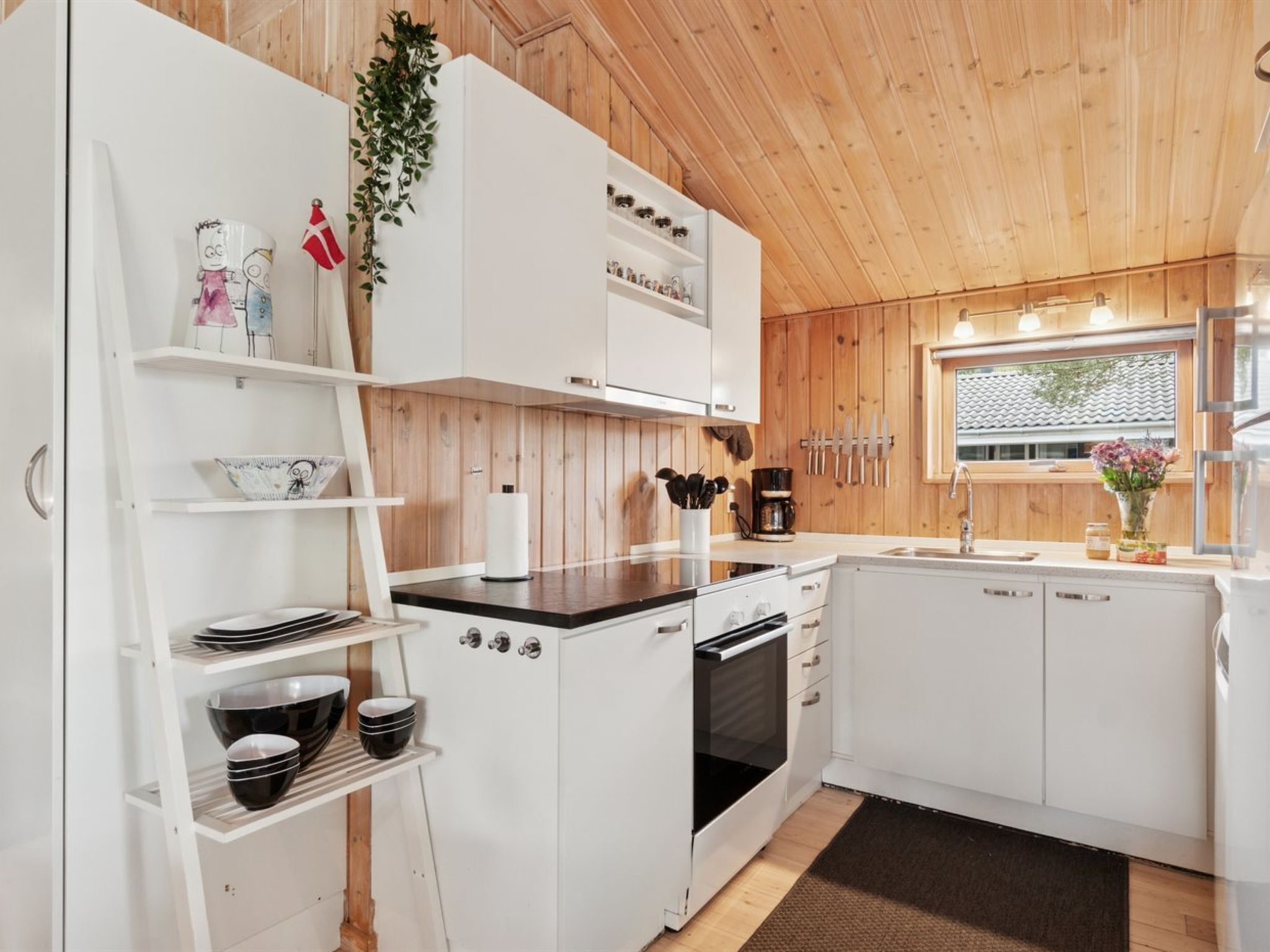 A modern kitchen with white cabinets, a black countertop, and a wooden ceiling.