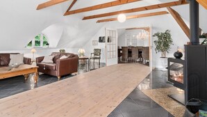 Un loft spacieux avec un plafond haut, des poutres apparentes, une grande table en bois au centre, une cheminée et un coin repas.