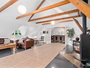 Ein großzügiger Loft mit hoher Decke, freiliegenden Holzbalken, einem zentralen Holztisch, einem Kamin und einem Essbereich.