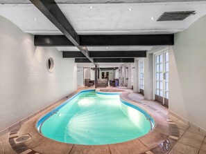 Ein großes, innenliegendes Schwimmbecken mit gewölbtem Design, umgeben von einem gefliesten Boden und Wänden sowie einer Decke mit freiliegenden Balken.