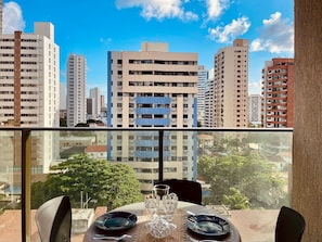 A dining area with a table set for two, overlooking a cityscape with high-rise buildings. - Beach Class Meireles by HostFácil (Fortaleza)