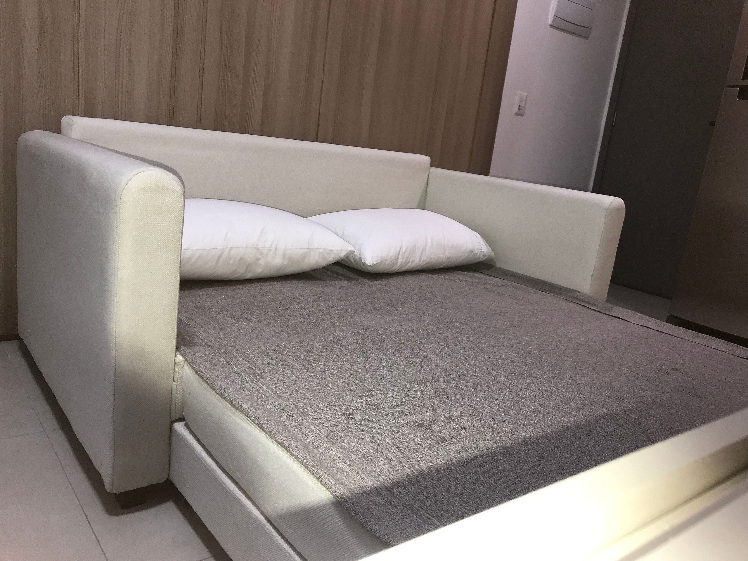 Una habitación moderna y minimalista con un sofá cama gris y dos almohadas blancas.