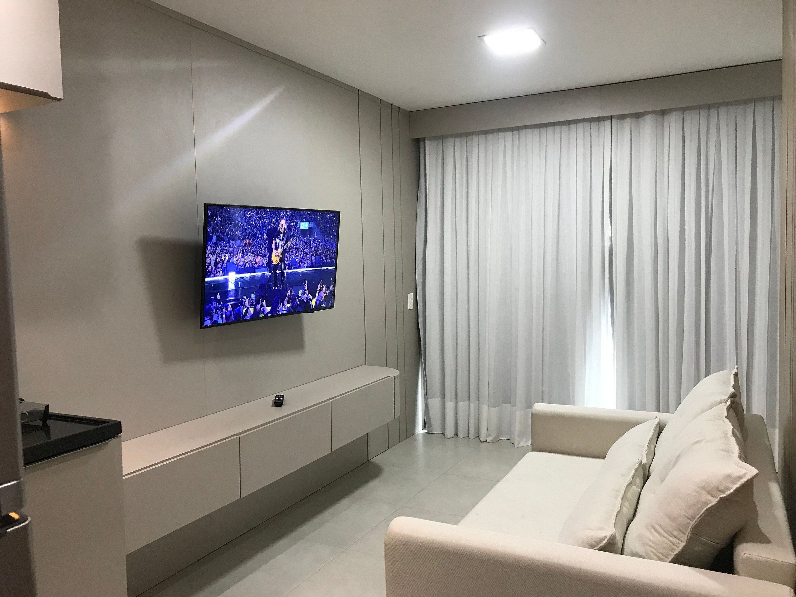 A modern living room with a flat-screen TV mounted on the wall, a sofa, and a large window with curtains.