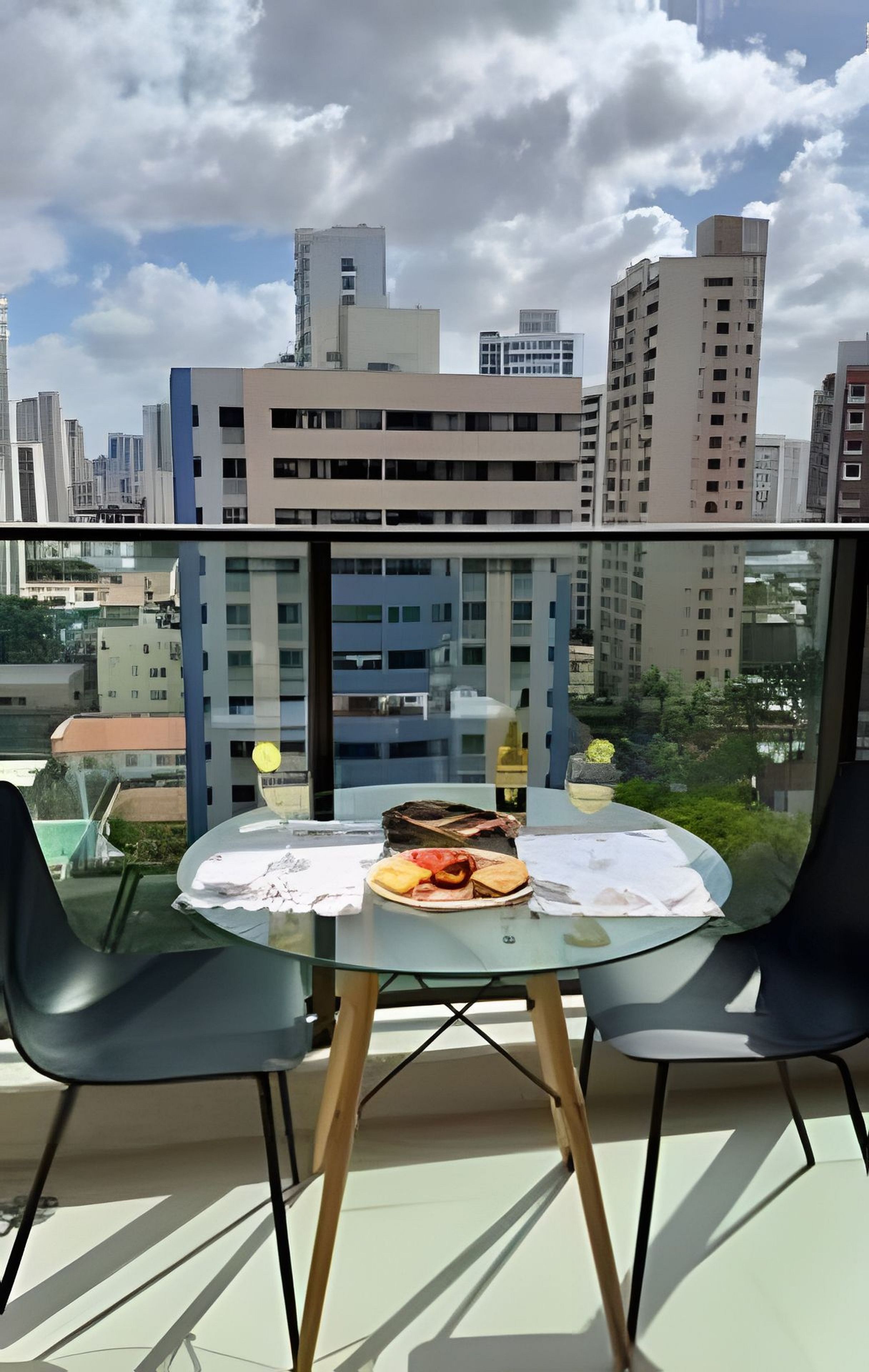 Ein Tisch mit Glasplatte und Stühle auf einem Balkon mit Blick auf eine Stadtlandschaft und verschiedene Gebäude.