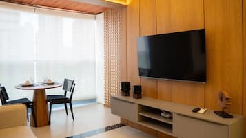Una sala de estar moderna con una televisión de pantalla plana montada en una pared de madera, una mesa de comedor con sillas y una pequeña mesa de centro.