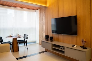 Uma sala de estar moderna com uma televisão de tela plana fixada numa parede de madeira, uma mesa de jantar com cadeiras e uma pequena mesa de centro.