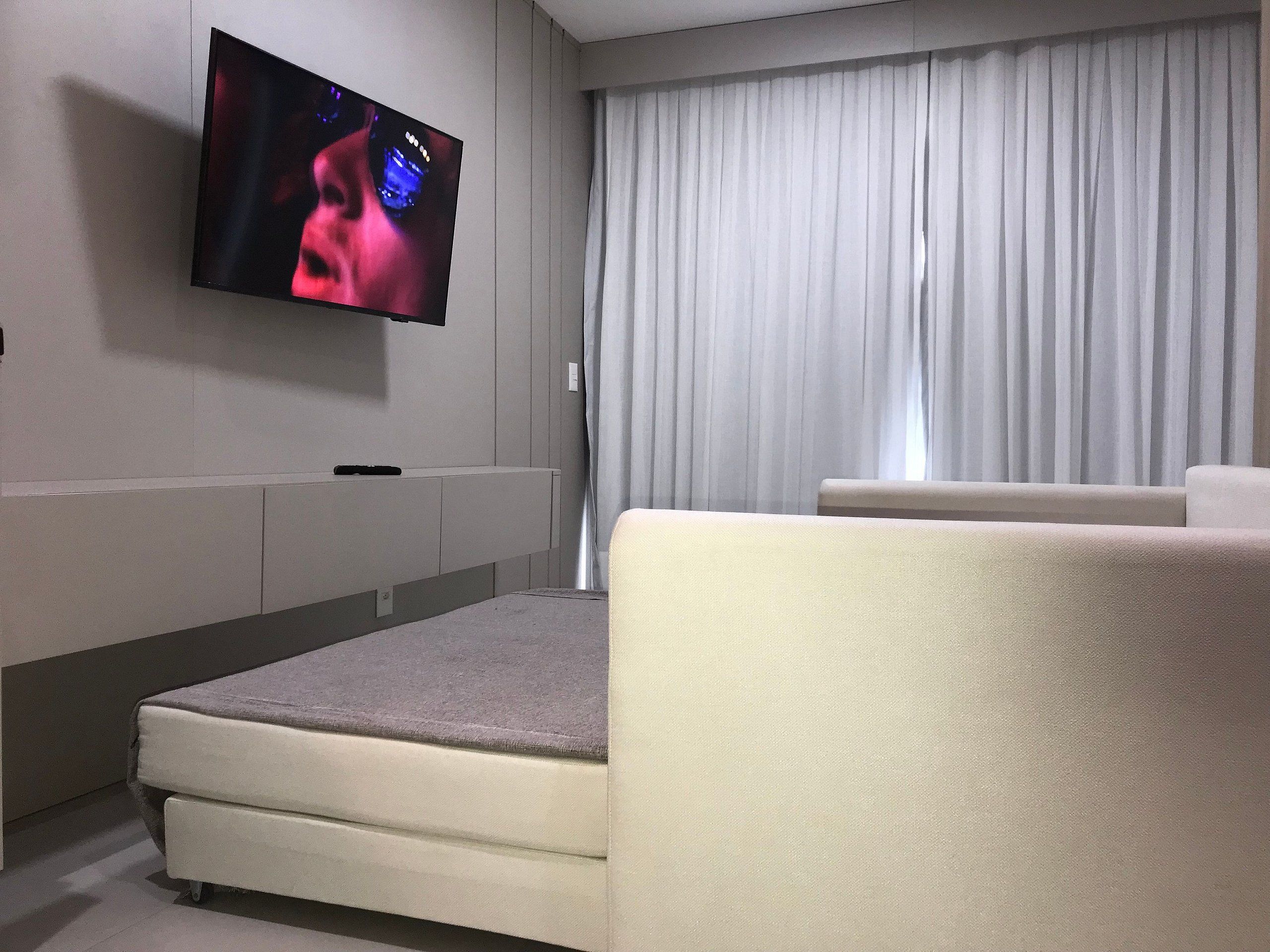 Una sala de estar moderna con un televisor de pantalla plana montado en la pared, un sofá y un ventanal con cortinas.