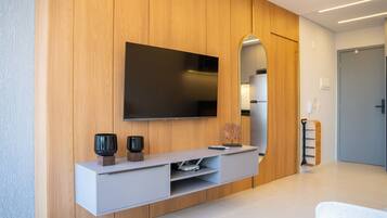 A modern living room with a flat-screen TV mounted on a wooden wall, a minimalist console table with decorative items, and a large mirror reflecting the room.