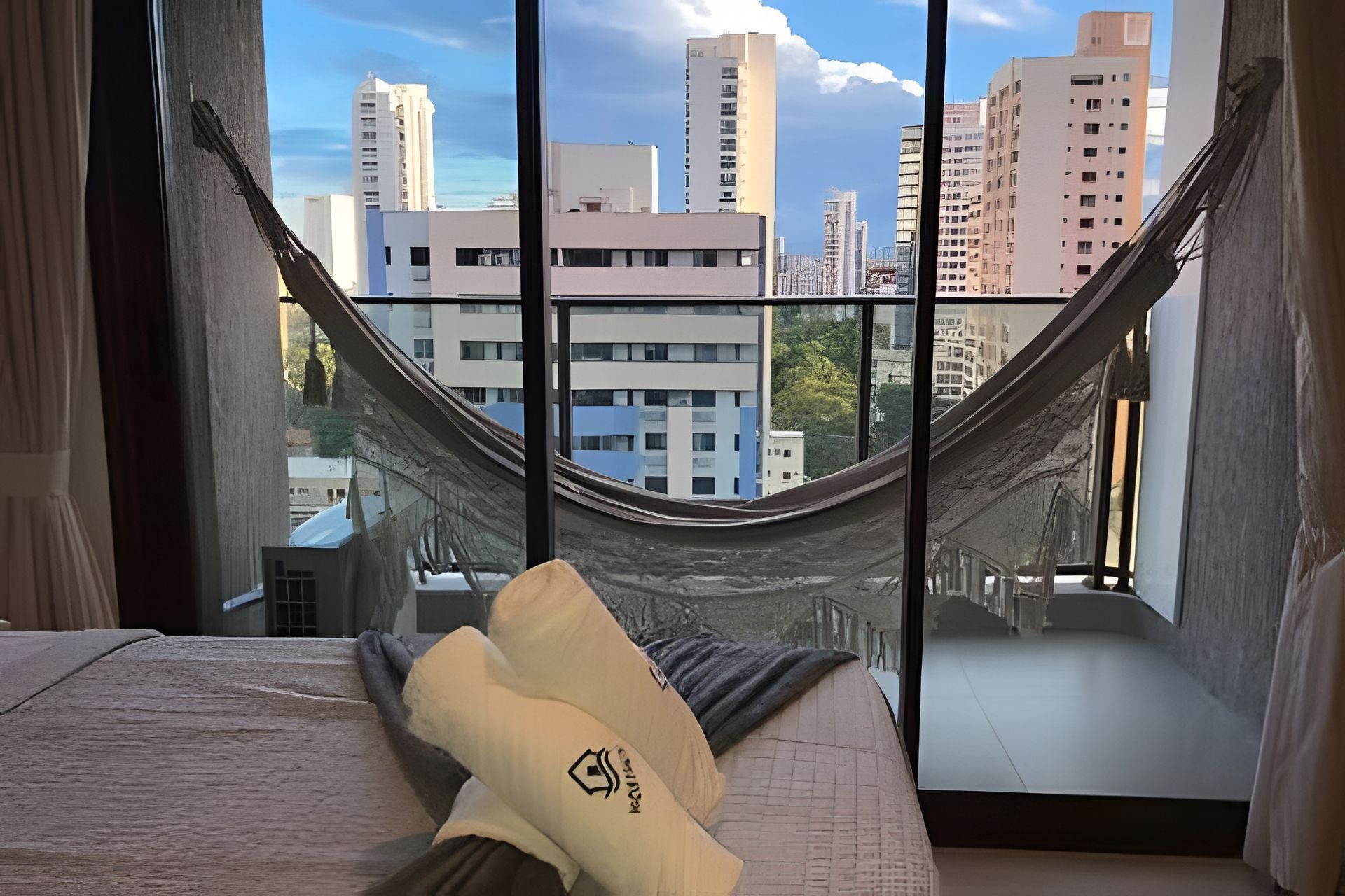 Una hamaca en una habitación con vistas a la ciudad, una cama con un almohadón y una ventana con cortinas.