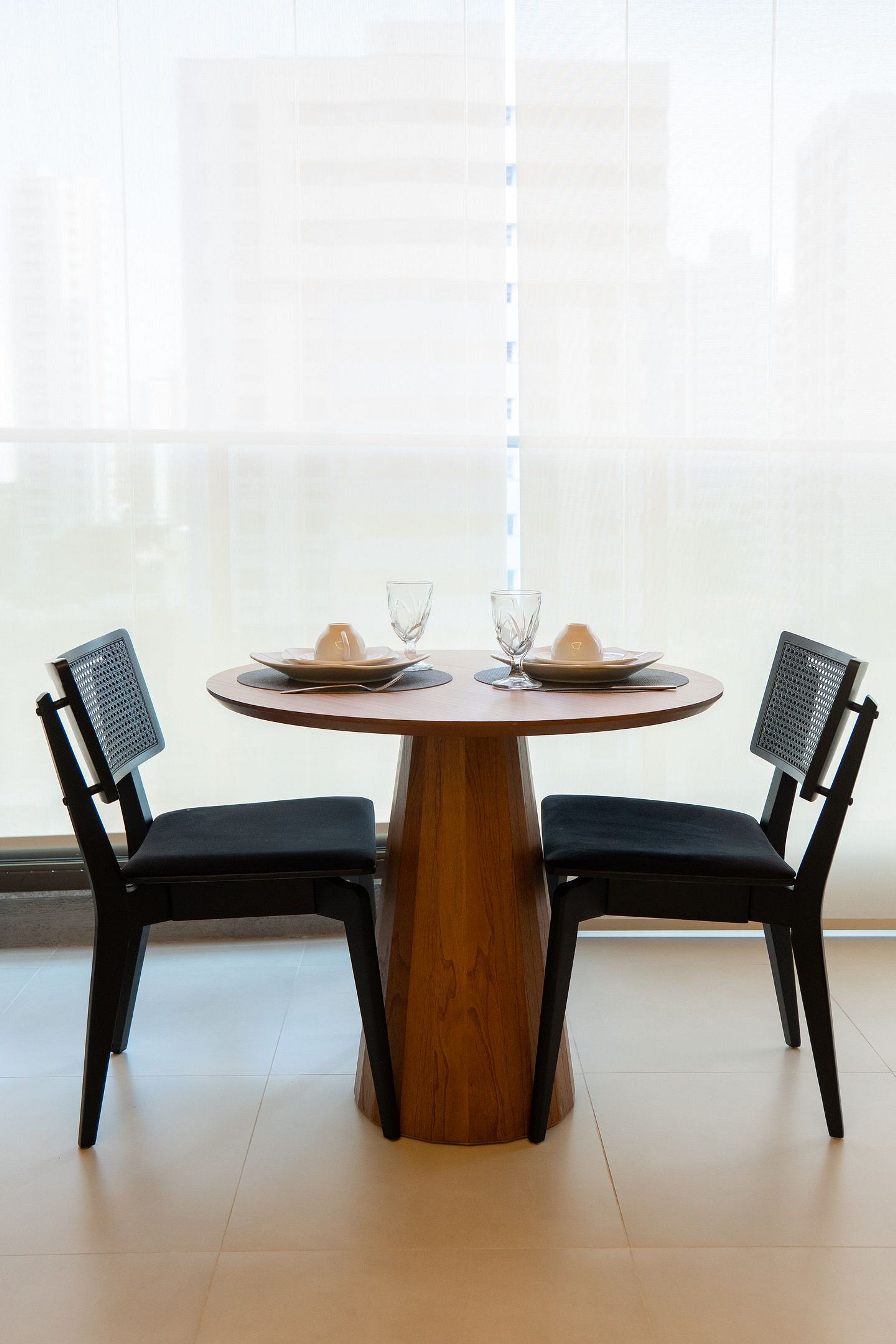 Uma mesa de jantar redonda com duas cadeiras, cada uma com encosto de tela, disposta com pratos, um copo e uma xícara.