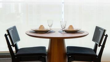 Uma mesa de jantar redonda com duas cadeiras, cada uma com encosto de tela, disposta com pratos, um copo e uma xícara.