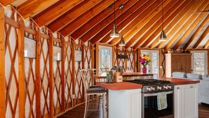 Una cocina con vigas de madera, una isla central, taburetes de bar, una estufa y lámparas colgantes.