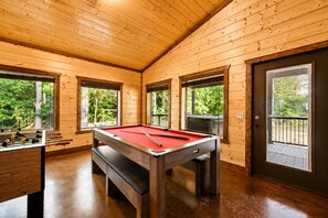 Una mesa de billar en una habitación con paredes de madera y ventanas grandes.