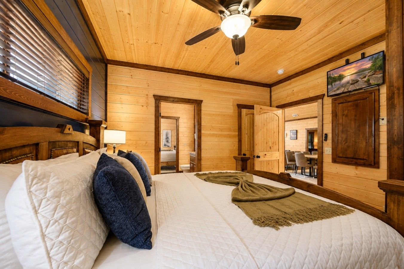 Een kamer met houten vloeren, een bed, een plafondventilator en een schilderij aan de muur.