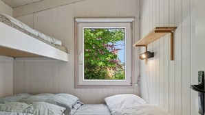 Una habitación con literas, una ventana con vistas a zonas verdes, un estante en la pared y una lámpara de noche.