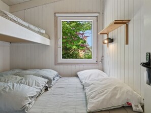 Ein Zimmer mit Etagenbett, einem Fenster mit Blick auf Grünflächen, einem Wandregal und einer Nachttischlampe.