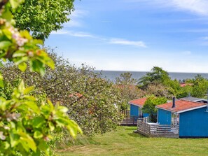 Ein Küstenanwesen mit freiem Blick auf das Meer, einer Holzdar Terrasse und einem kleinen Gebäude mit rotem Dach.