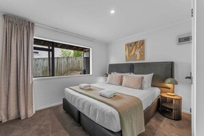 Ein Schlafzimmer mit Bett, Nachttischlampe, einem Fenster mit Vorhängen und einem Wandbild.