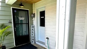 A house entrance with a black door labeled 'GRANNY SUITE STUDIO,' a welcome sign, and a hose connected to the door.