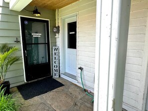 A house entrance with a black door labeled 'GRANNY SUITE STUDIO,' a welcome sign, and a hose connected to the door.