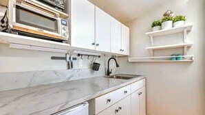 A kitchen with white cabinets, a marble countertop, a built-in microwave, and a hanging pot rack.