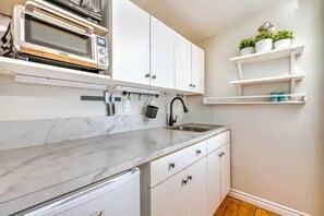 A kitchen with white cabinets, a marble countertop, a built-in microwave, and a hanging pot rack.