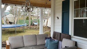 A covered porch with a wooden bench, a sofa with cushions, and a chandelier.