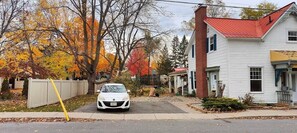 A residential street with houses, a parked car, and autumn-colored trees.