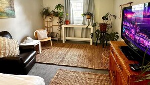 A living room with a sofa, a TV, a wooden cabinet, and potted plants. - 2 bed Suite: kitchen, parking, king/queen upstairs (Carleton Place)
