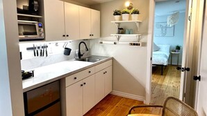 A compact kitchen with white cabinets, a microwave, and a sink. There is a small dining area with a table and a chair. - 2 bed Suite: kitchen, parking, king/queen upstairs (Carleton Place)