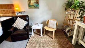 A cozy living room with a black leather sofa, a small white table, a wooden chair, a painting on the wall, and a plant. - 2 bed Suite: kitchen, parking, king/queen upstairs (Carleton Place)