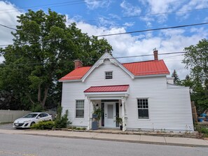 A white two-story house with a red roof, a front porch, and a garage door.