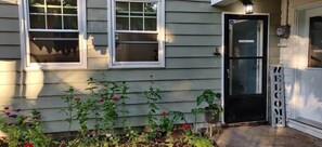 A house with a black door labeled 'GRANNY SUITE,' a welcome sign, and a garden with various plants.