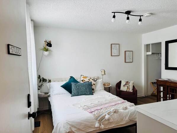 A bedroom with a bed, bedside table, lamp, chair, and a door labeled 'STUDIO'.