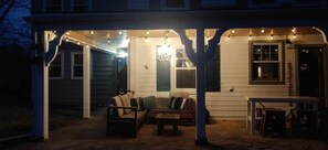 A covered porch with string lights, a chandelier, and outdoor furniture.