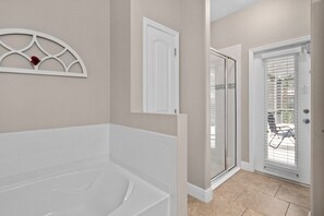Ein Badezimmer mit Badewanne, Dusche und einer Glastür zu einem Außenbereich.