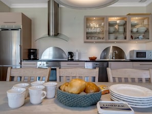 A modern kitchen with stainless steel appliances, a built-in oven, and a microwave. There are white mugs and a basket of croissants on the table. - "Verner" - 990m from the sea by Interhome (Skagen)