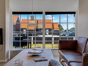 A room with a large window, a table with magazines, a sofa, and a hanging light fixture. - "Verner" - 990m from the sea by Interhome (Skagen)