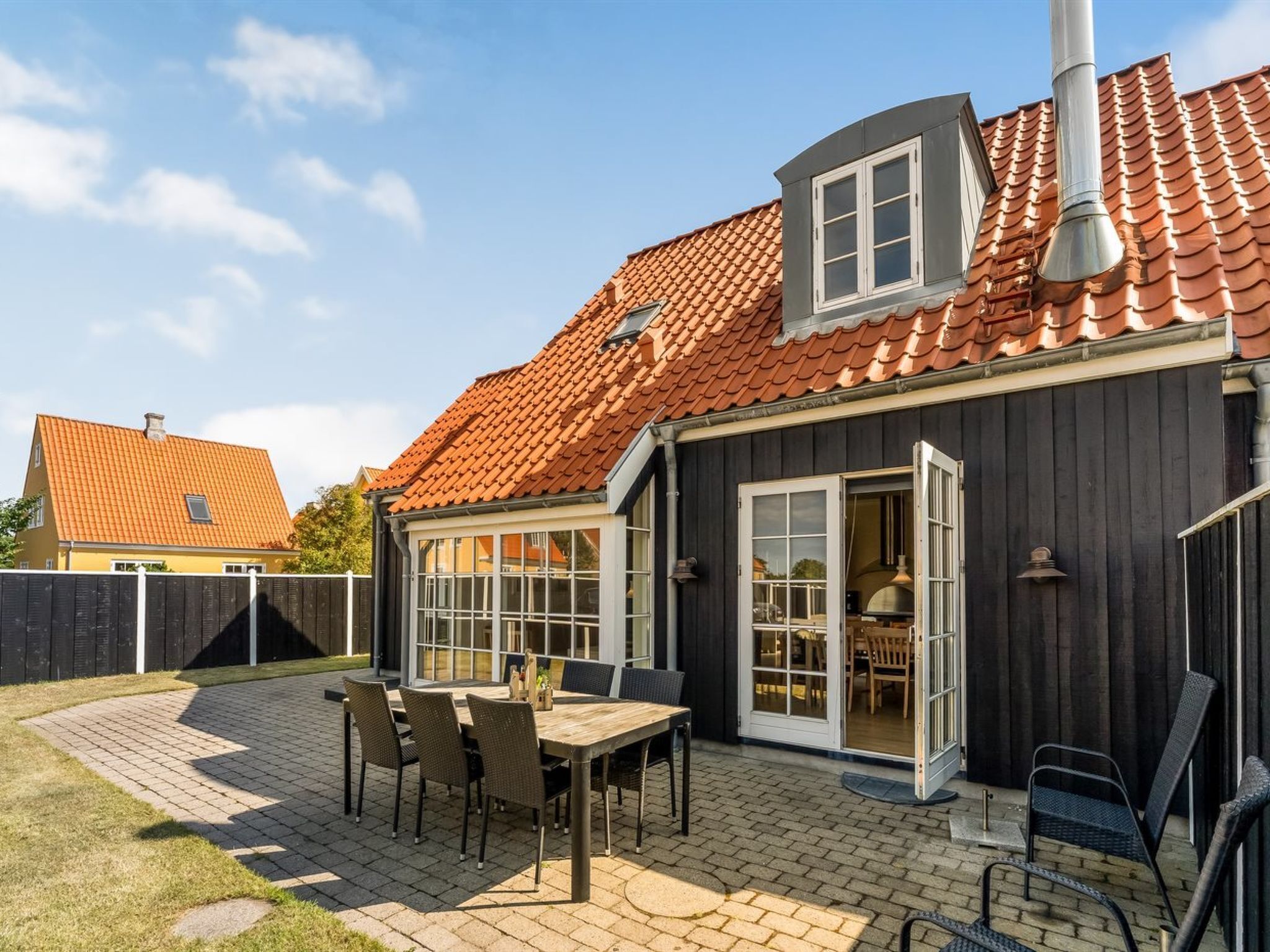 A house with a tiled roof, a patio with a table and chairs, and a dark exterior wall.