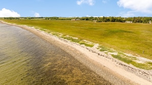 Eine Küstenlandschaft mit blauem Himmel, Sandstrand und einer grünen Wiese.