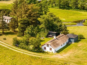 Ein weißes Haus mit einem Reetdach, umgeben von üppiger Vegetation und einem kleinen Teich.