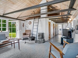 Ein großzügiger Wohnbereich mit hoher Decke, Kamin, Fernseher und Blick ins Freie.