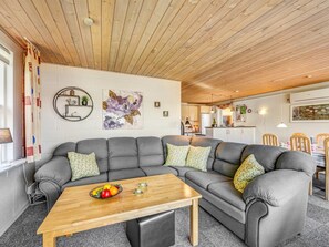 Ein modernes Wohnzimmer mit einer Eckcouch, einem Holztisch und einer Küche im Hintergrund.