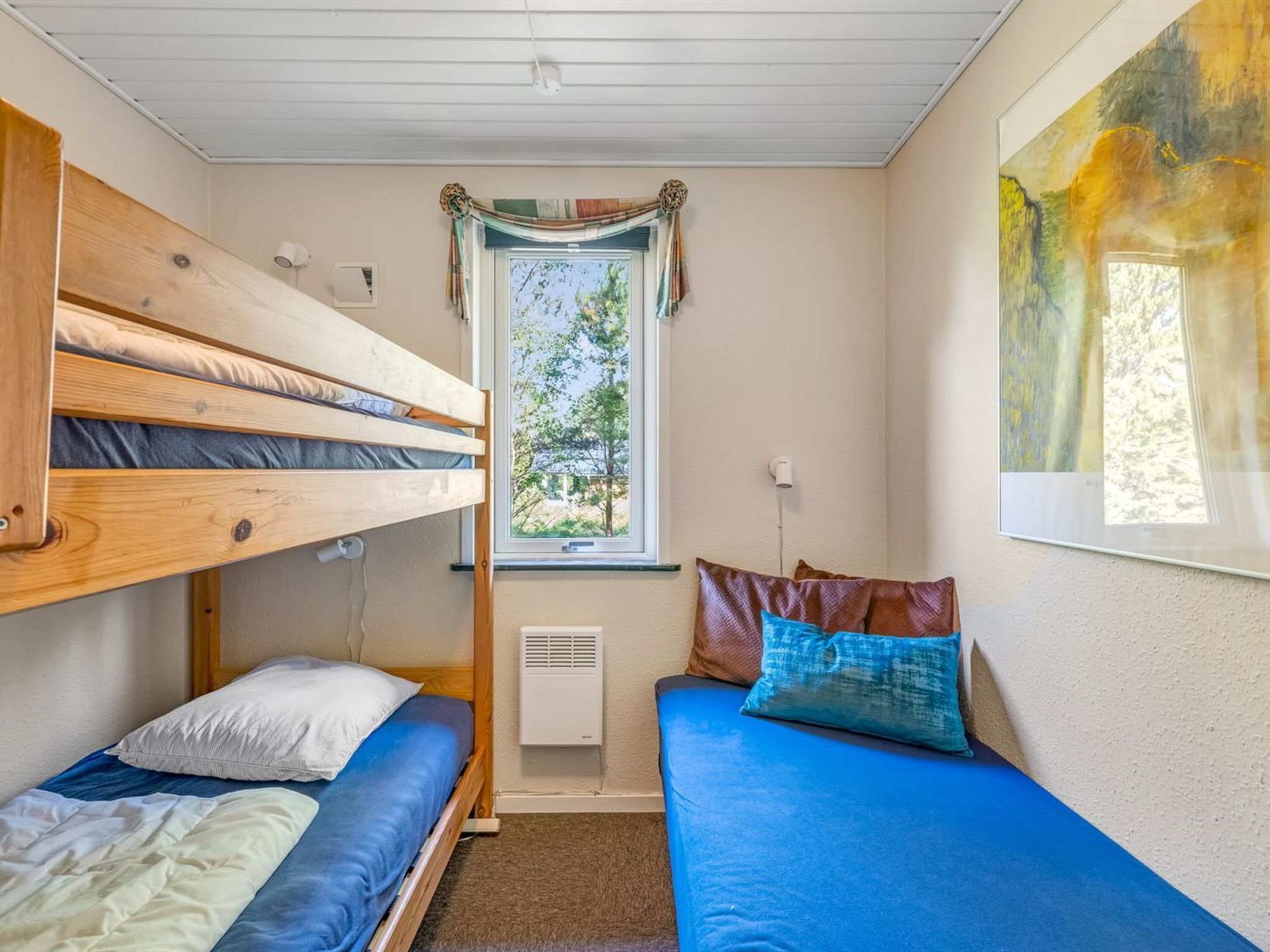 A room with bunk beds, a window with curtains, a radiator, and a painting on the wall.