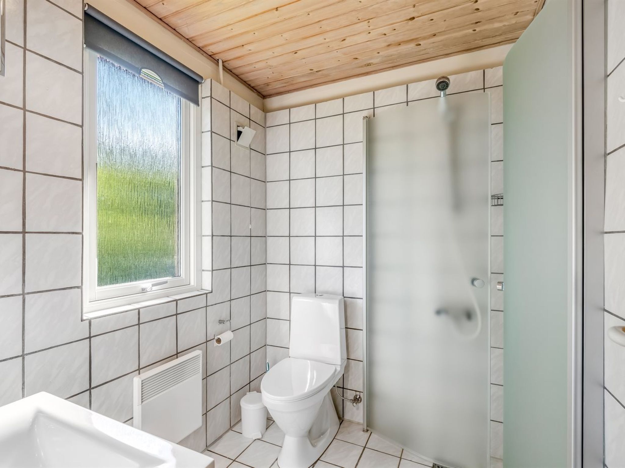Un baño con ducha, inodoro y lavamanos, paredes con azulejos y una ventana con vistas a zonas verdes.
