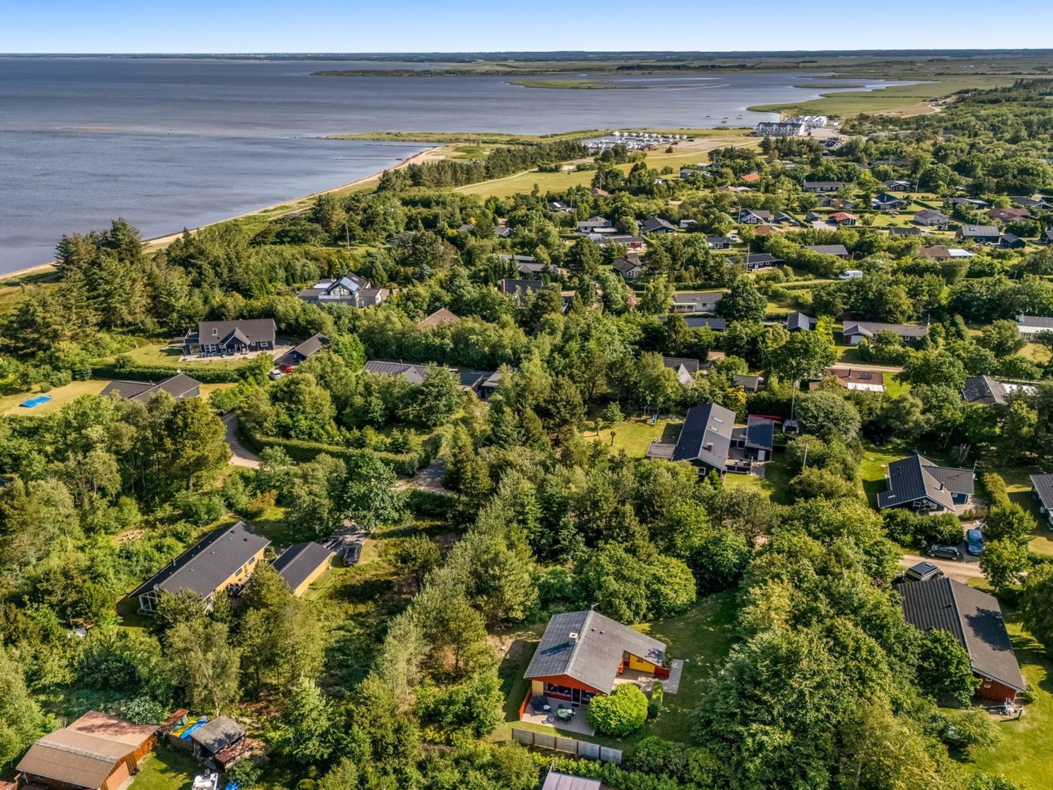 Vista aerea di una zona residenziale con case circondate da vegetazione lussureggiante e un ampio specchio d'acqua sullo sfondo.