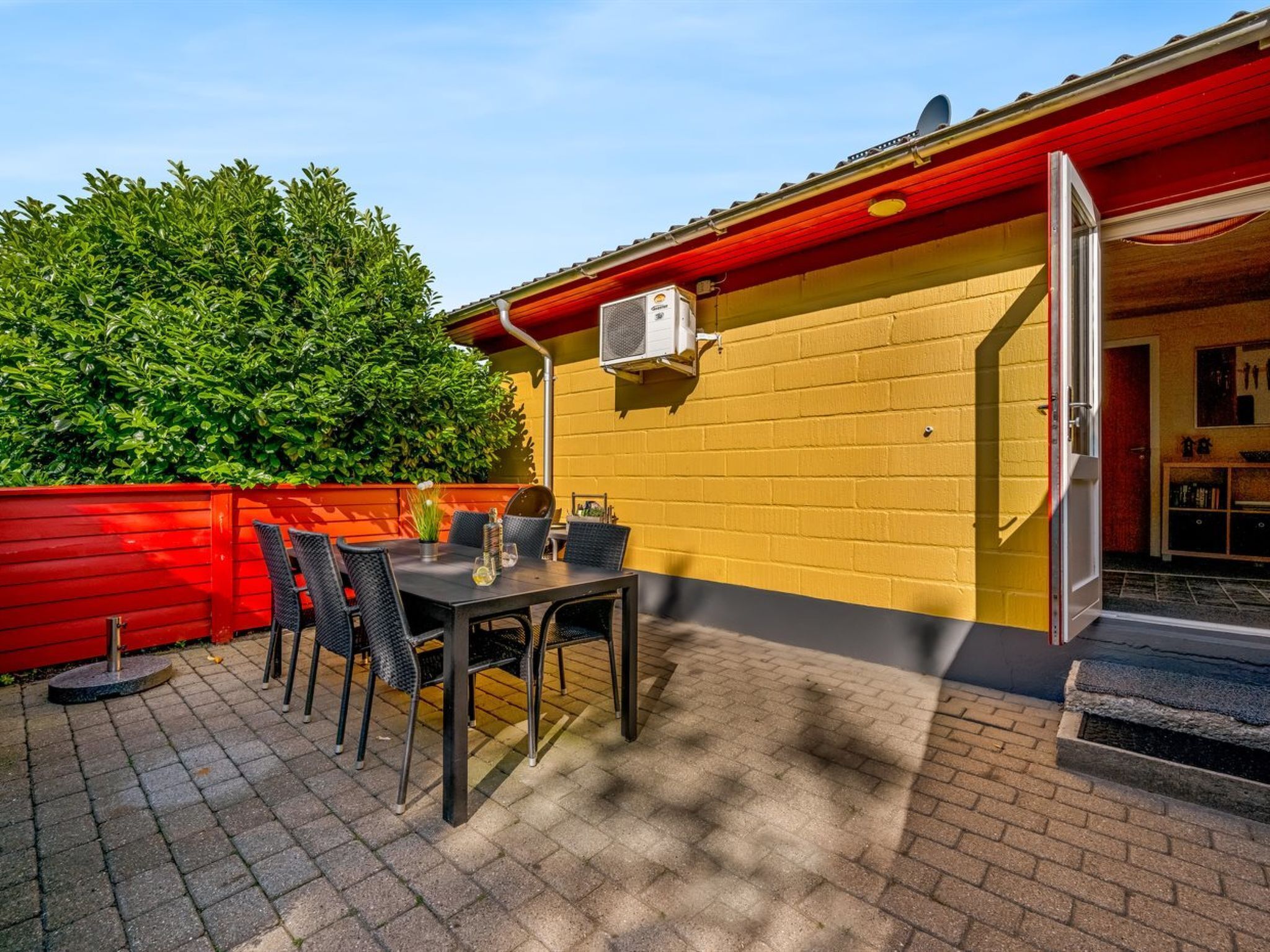 A patio with a table and chairs, a red fence, and a yellow wall.