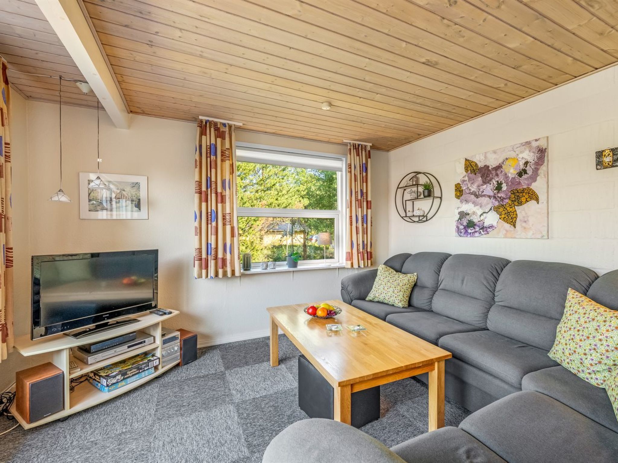 Een woonkamer met een bank, een salontafel, een televisie en een raam met gordijnen.