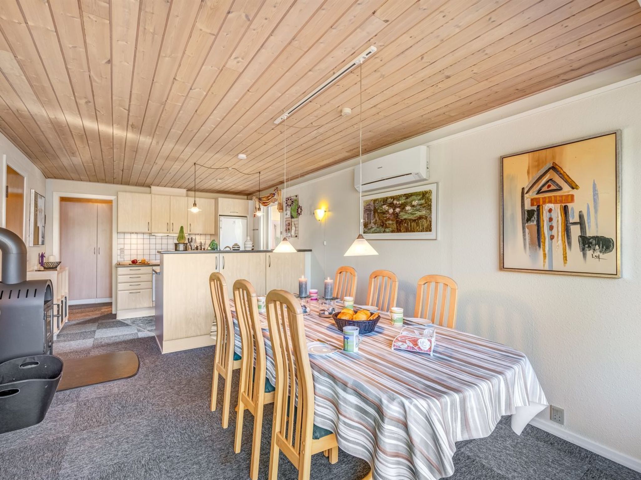 Un comedor con mantel a rayas, sillas de madera y una cocina al fondo.